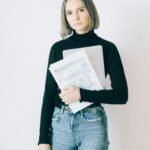 Young woman confidently holding tax paperwork against a white backdrop.